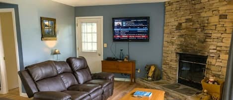 A living room with a stone fireplace, leather sofas, a flat-screen TV, and a wooden coffee table.