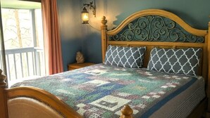 A bed with a quilt, a wall-mounted lamp, and a window with curtains. - Hillbilly Hilton 2 Bedroom Chalet (Pigeon Forge)