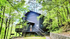 A modern, multi-level cabin with a staircase leading to the entrance, surrounded by dense forest. - Hillbilly Hilton 2 Bedroom Chalet (Pigeon Forge)