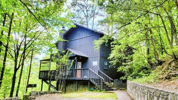 Eine moderne, mehrstöckige Holzhütte mit einer Treppe zum Eingang, umgeben von dichtem Wald.