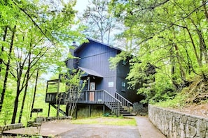 A modern, multi-level cabin with a staircase leading to the entrance, surrounded by dense forest. - Hillbilly Hilton 2 Bedroom Chalet (Pigeon Forge)