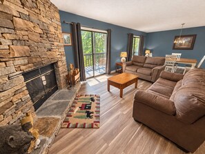 A living room with a stone fireplace, a brown leather sofa, a wooden coffee table, and a rug with animal prints. - Hillbilly Hilton 2 Bedroom Chalet (Pigeon Forge)