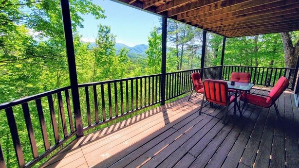 Una terraza de madera con una mesa y sillas, rodeada por una barandilla, con vistas a un paisaje boscoso.
