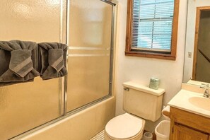 Baño con ducha, inodoro, lavamanos y ventana con persianas.