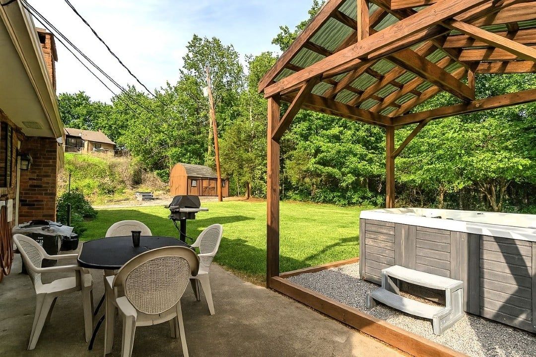 An outdoor patio with a wooden pergola, a hot tub, and a barbecue area.