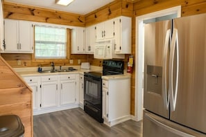 A compact kitchen with white cabinets, a stove, a microwave, and a stainless steel refrigerator. - Hoot N Holler 5 Bedroom Chalet (Pigeon Forge)