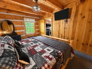 A wooden cabin bedroom with a bed, a mirror, a television, and a window. - Blu's Blessed View 1 Bedroom Cabin (Sevierville)