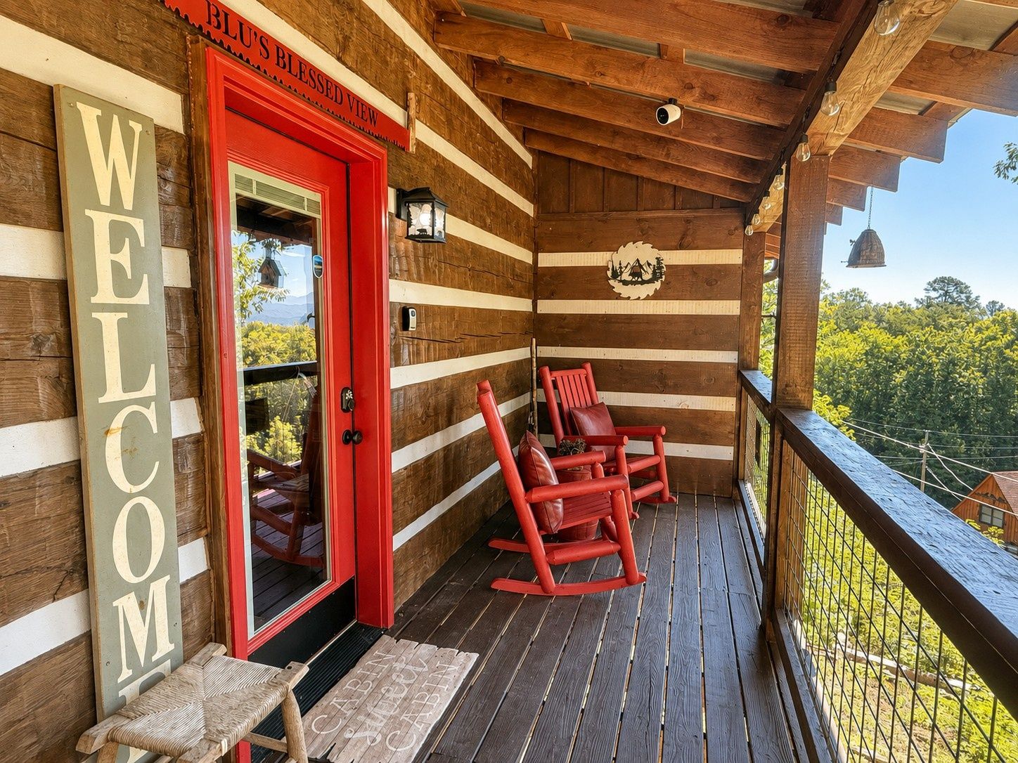 Una cabaña de madera con puerta roja, un letrero de bienvenida y una mecedora en el porche.