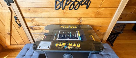 Una máquina arcade de Pac-Man en una habitación de madera con un cartel que dice 'Blessed'.