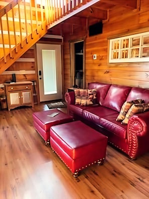 A wooden interior with a red leather sofa, ottoman, and a staircase. - Blu's Blessed View 1 Bedroom Cabin (Sevierville)