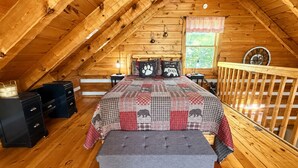 Ein gemütliches Schlafzimmer im Dachgeschoss mit schrägen Wänden, einem Bett mit karierter Bettdecke, einer Sitzbank und Holzmöbeln.