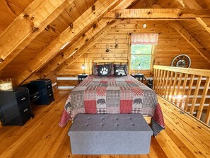 A cozy attic bedroom with a sloped ceiling, a bed with a checkered quilt, a bench, and wooden furniture. - Blu's Blessed View 1 Bedroom Cabin (Sevierville)