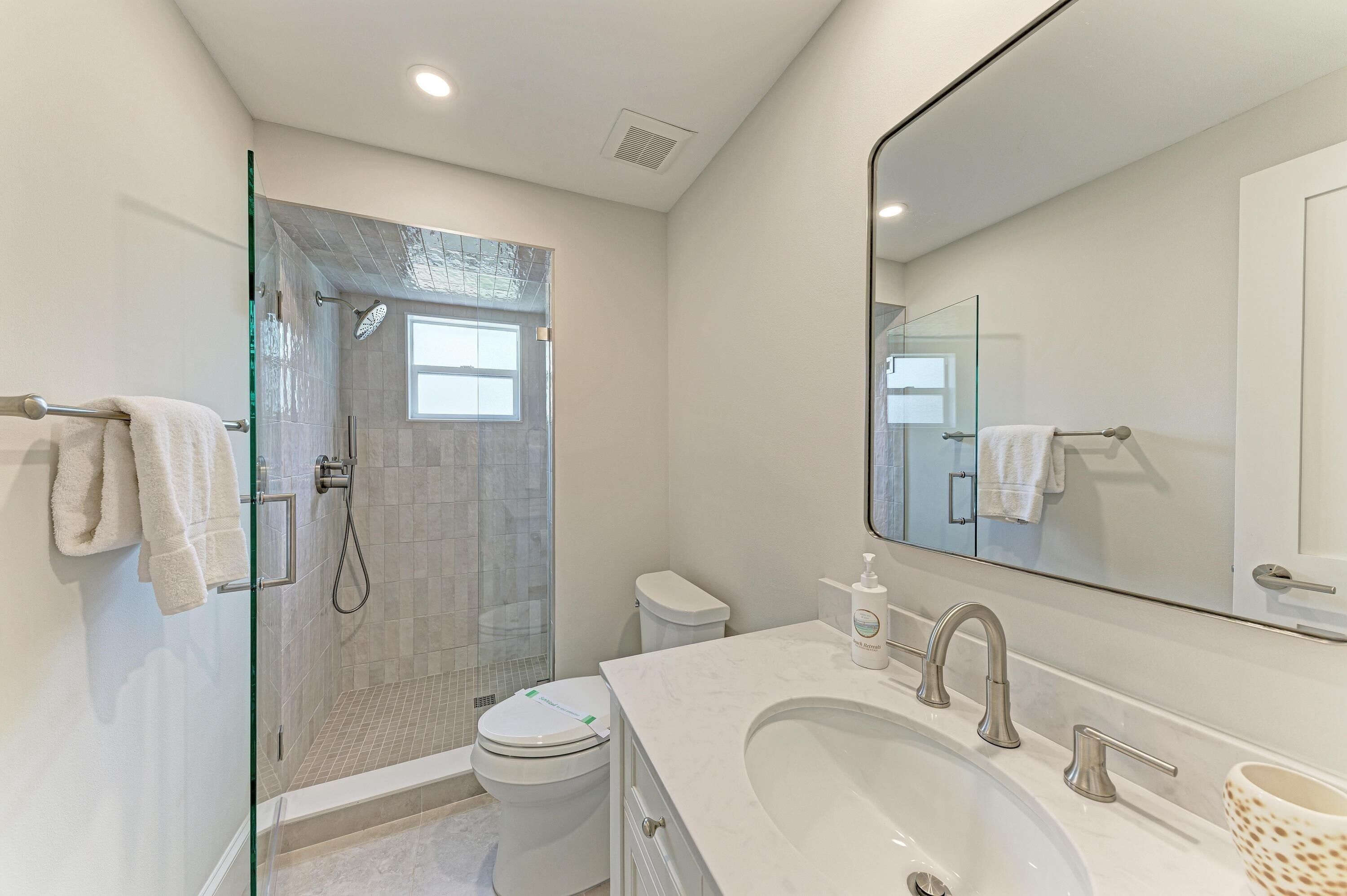 A modern bathroom with a glass shower enclosure, a toilet, a sink with a large mirror, and a towel rack.