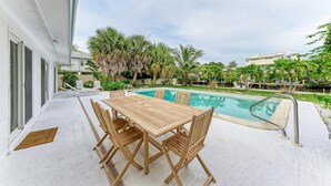 Ein Poolbereich mit Holztisch und -stühlen, einem Schwimmbecken und umgebender Bepflanzung.