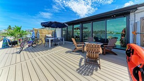 Una terraza de madera con muebles de exterior, una bicicleta y vista al mar a través de grandes ventanales.