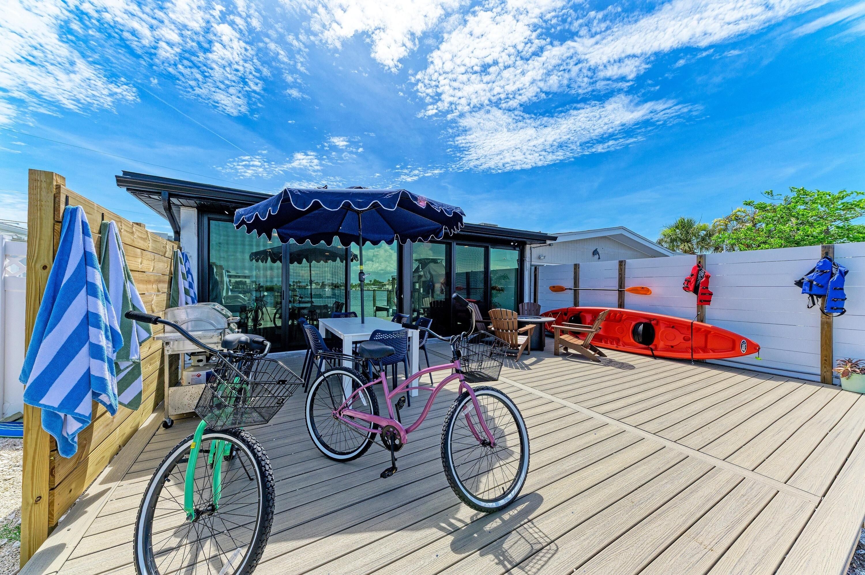 Une terrasse en bois avec un vélo, un kayak rouge et un espace salon abrité.