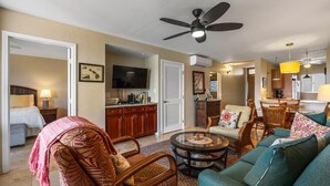 A spacious living room with a television, a ceiling fan, and a dining area with chairs and a table. - Menehune Shores, #507 2 Bedroom Condo (Kihei)