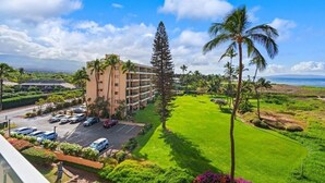 A hotel with a parking lot, a grassy area with palm trees, and a view of the ocean. - Menehune Shores, #507 2 Bedroom Condo (Kihei)
