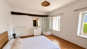 Une chambre avec un grand lit, une douche à l’italienne, une commode et une fenêtre.