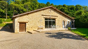 Un bâtiment en pierre avec une porte en bois, de grandes fenêtres et une allée gravillonnée.
