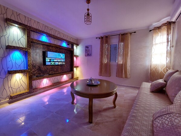 A living room with a flat-screen TV, a coffee table, a sofa, and patterned walls.