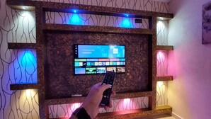 Een aan de muur bevestigde televisie, een afstandsbediening in de hand van een persoon.