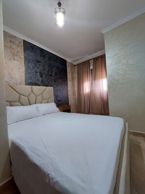 A hotel room with a bed, a nightstand, a wall with a textured design, and a ceiling light.