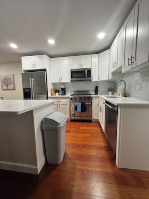 A modern kitchen with white cabinets, a stainless steel refrigerator, a microwave, an oven, and a sink.