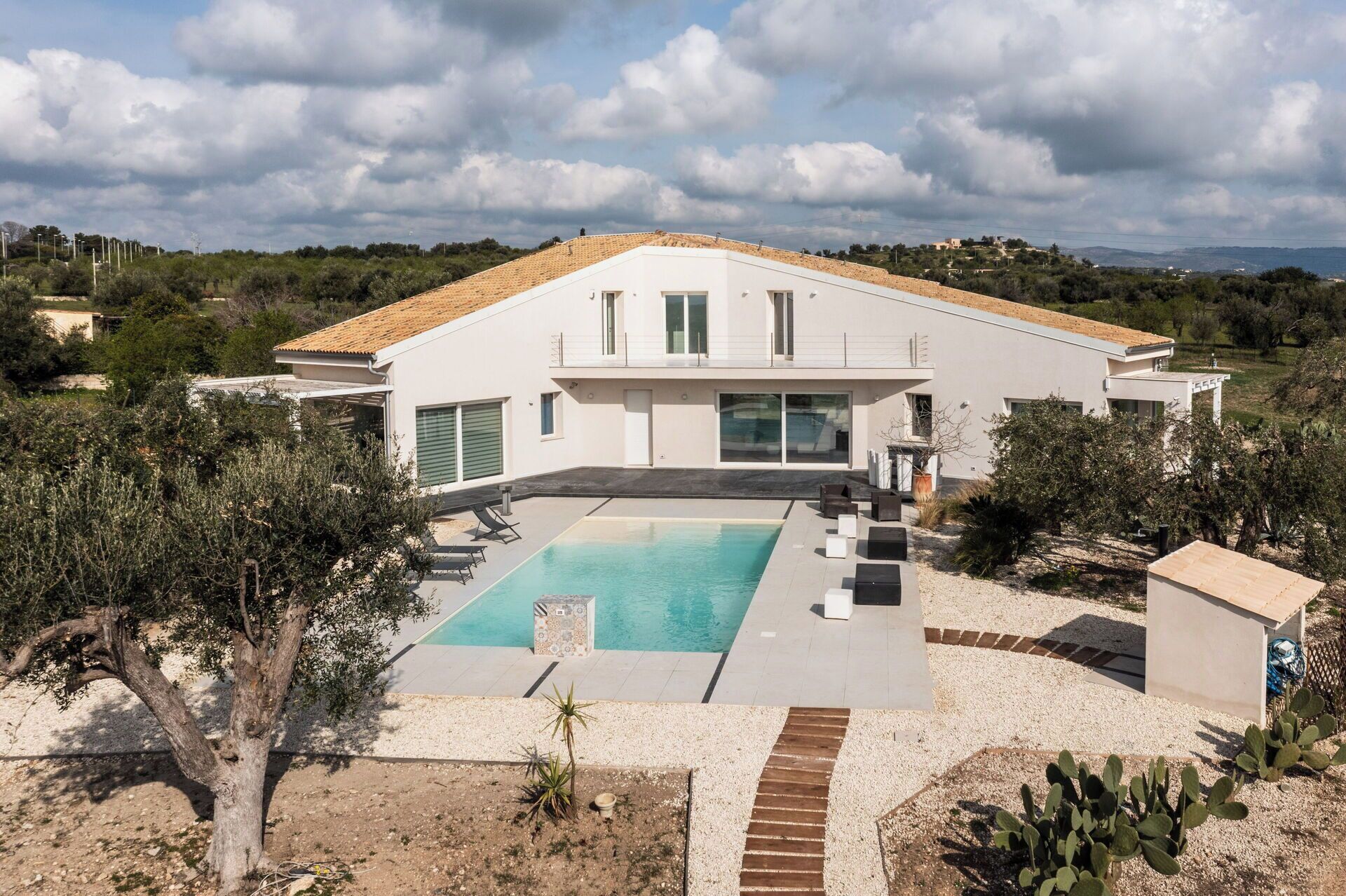 A modern villa with a swimming pool, a covered patio, and a view of the surrounding landscape.