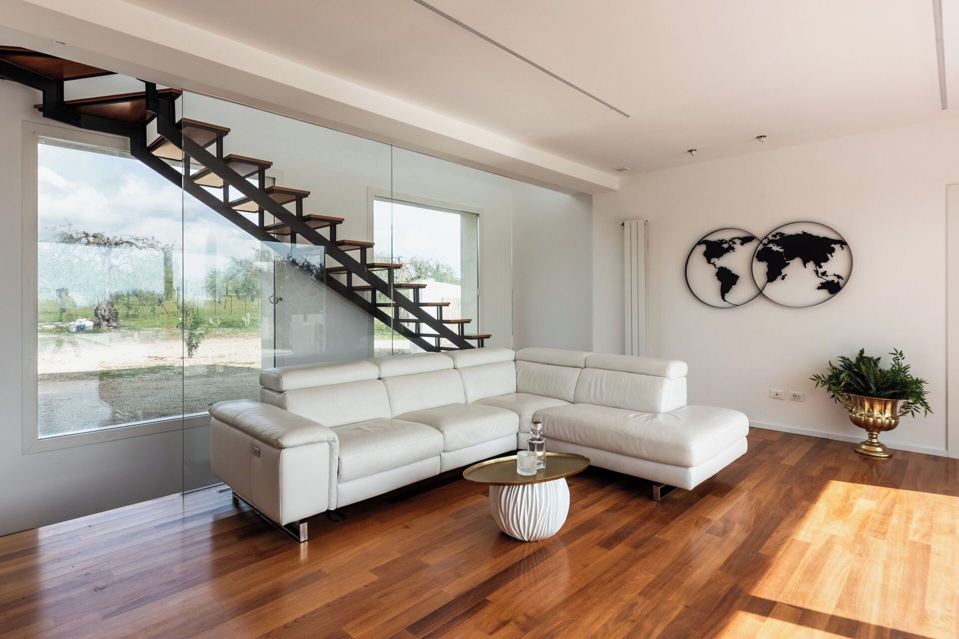 Een moderne woonkamer met een grote witte hoekbank, een houten trap en een wereldkaart als kunstwerk aan de muur.