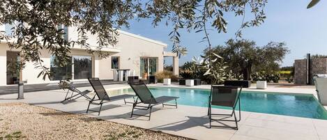 A modern pool area with lounge chairs, a swimming pool, and a building with large windows.