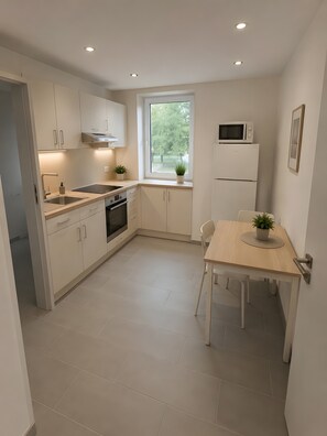 Une cuisine moderne avec des meubles blancs, un four encastré, un four à micro-ondes et un coin repas comprenant une table et des chaises.