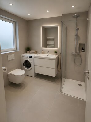 Ein modernes Badezimmer mit Waschmaschine, Toilette, Waschbecken und Dusche.