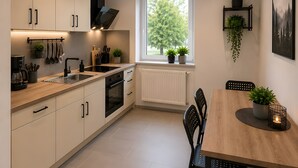 Eine moderne Küche mit Essbereich, ausgestattet mit einem großen Fenster, weißen Schränken und einem Holztisch.