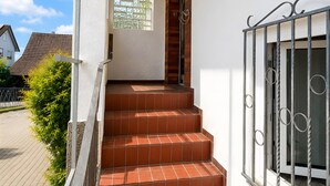 Eine Treppe führt zu einer Tür mit einem Fenster, einem Metallgeländer und Blick auf die Straße.