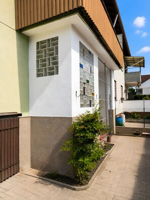 Un immeuble résidentiel à la façade blanche, au toit brun et doté d’un petit jardin agrémenté d’un arbuste.