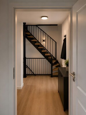 Un intérieur moderne avec un escalier en bois, une porte blanche et une petite plante posée sur un comptoir.