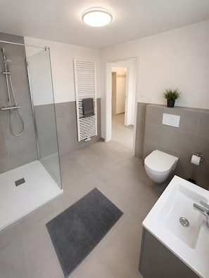 Ein modernes Badezimmer mit Dusche, Toilette, Waschbecken und einer Topfpflanze.