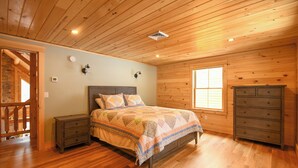 Une chambre à coucher aux murs lambrissés, avec un lit, des tables de chevet, une commode et une fenêtre.