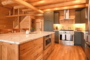 Eine Küche mit Holzausstattung, einer Granitabdeckung, Edelstahlgeräten und einer Holztreppe.
