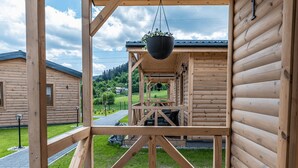 Een houten chalet met een veranda, een hangplant en uitzicht op een groen landschap.