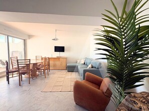 A living room with a sofa, chairs, a coffee table, a TV, and a large plant. - 011 / GRAND T3 RESIDENCE LE FRANCE (Sète)