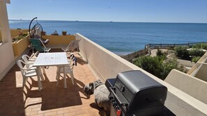 Eine Terrasse mit Tisch, Stühlen, einem Grill und Meerblick.