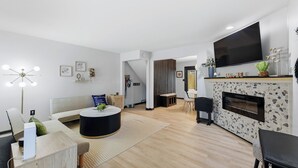 Een moderne woonkamer met een bank, salontafel, open haard, televisie en een eethoek.