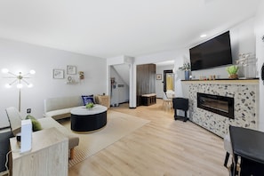 A modern living room with a sofa, coffee table, fireplace, TV, and a dining area.