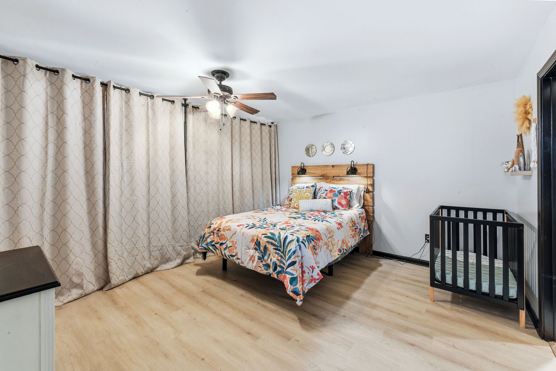 Une chambre à coucher comprenant un lit, un berceau, un ventilateur de plafond et une étagère murale décorative.