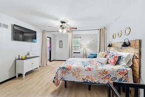 Une chambre avec un lit, un bureau, un ventilateur de plafond et un téléviseur.