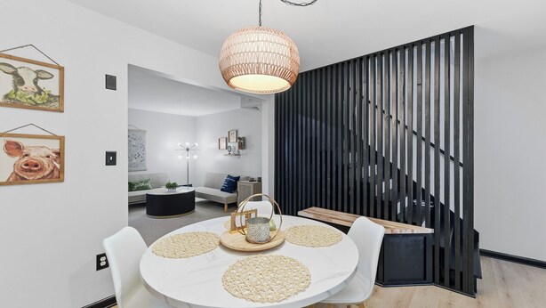 Een eetruimte met een ronde tafel, witte stoelen, een geweven hanglamp en een zwart scheidingswandje.