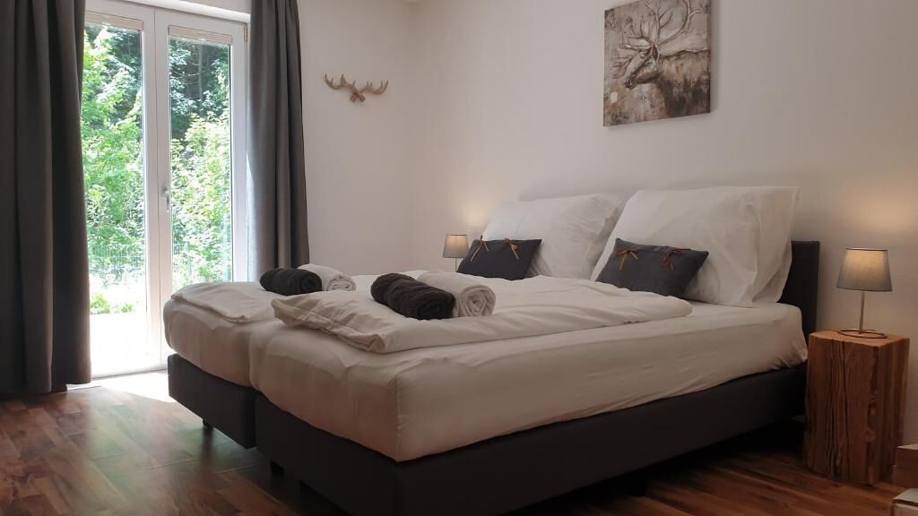 Ein Doppelbett mit weißen Leinentüchern, zwei Nachttische mit Lampen, eine Dekoration aus Hirschgeweihen und ein Gemälde an der Wand.