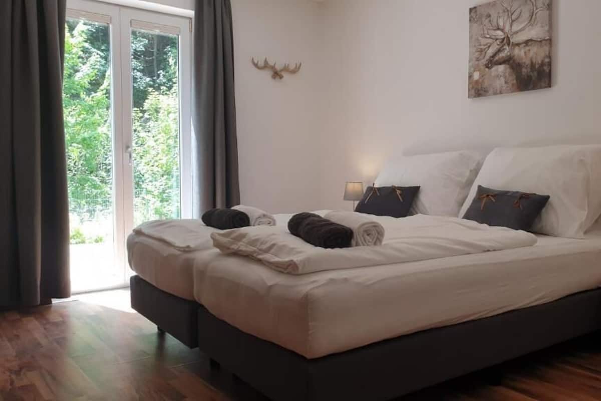 Ein Doppelbett mit weißen Leinentüchern, zwei Nachttische mit Lampen, eine Dekoration aus Hirschgeweihen und ein Gemälde an der Wand.
